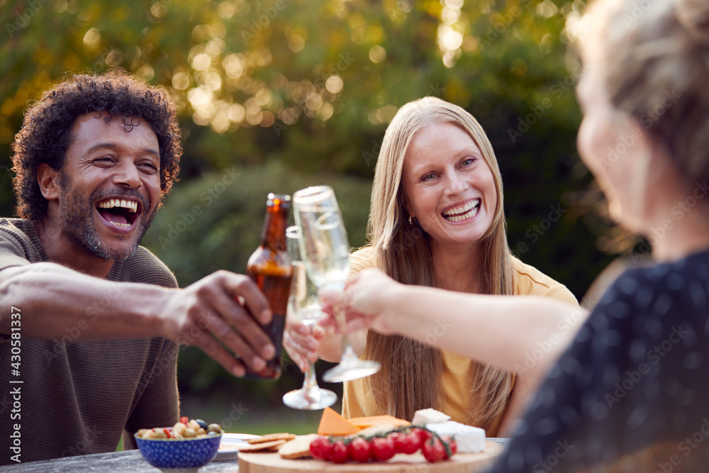 Group Of Friends Celebrating With Beer And Champagne As They Sit At Table In Garden With Snacks Group Of Friends Celebrating With Beer And Champagne As They Sit At Table In Garden With Snacks