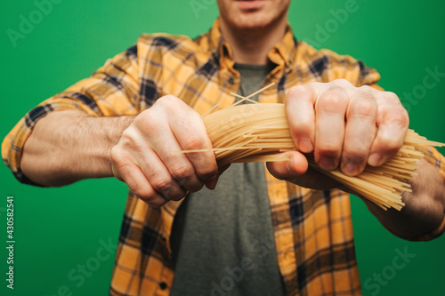 Close up young man strongly breaks spaghetti, isolated on green background