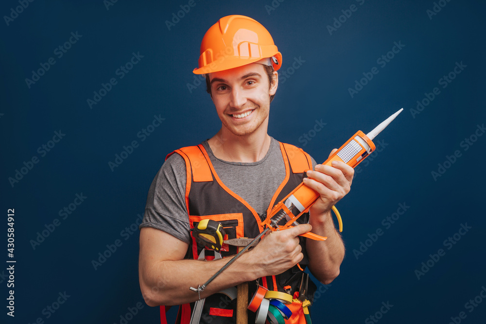 Happy builder holds construction adhesive, isolated over blue background
