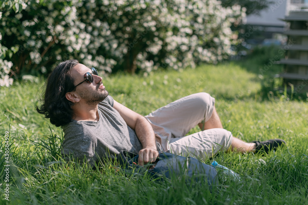 A man sits on the grass in a blooming park in a big city.