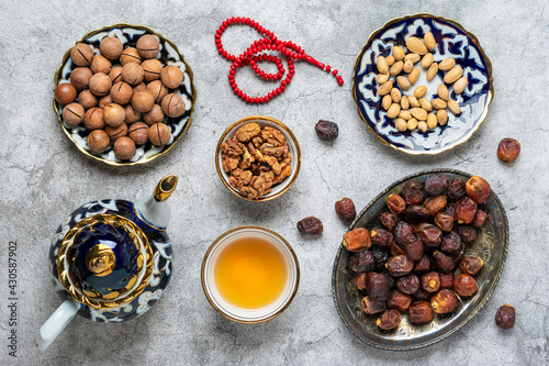 Popular food during Iftar - macadamia nuts, pistachios, walnuts, dry dates. Karan, rosary, teapot, bowl with black tea on concrete background Top view Flat lay Muslim holiday of holy month of Ramadan
