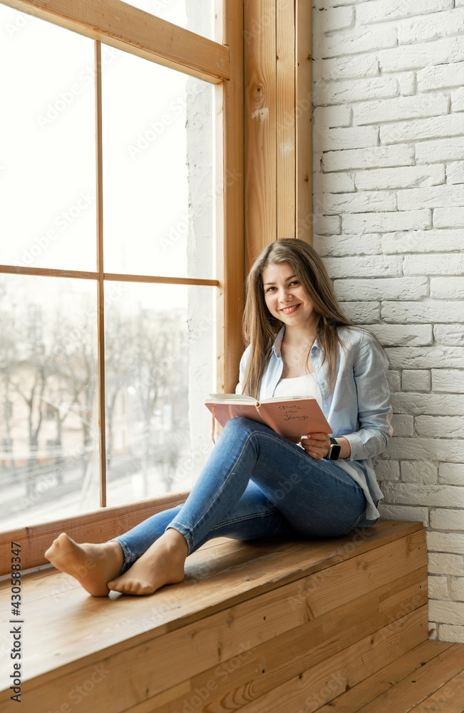 young girl student sitting by the window holding a diary and a pen. Beautiful female hands writing an entry in the diary with an ink fountain pen. young girl student sitting by the window holding a diary and a pen. Beautiful female hands writing an entry in the diary with an ink fountain pen.