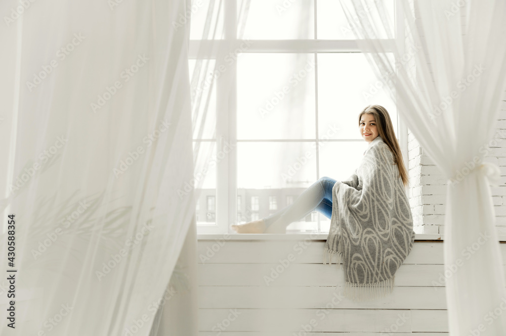 happy female student sitting by the window holding a cup of coffee. a young girl was dreaming looking out the window. house insulation happy female student sitting by the window holding a cup of coffee. a young girl was dreaming looking out the window. house insulation