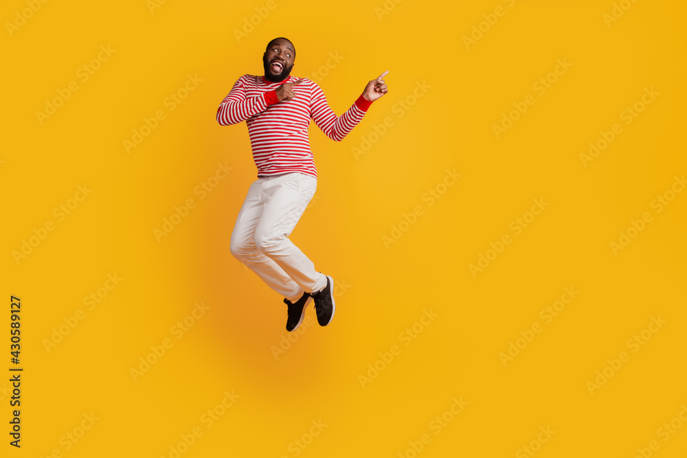 Handsome man jumping direct fingers empty space on yellow background