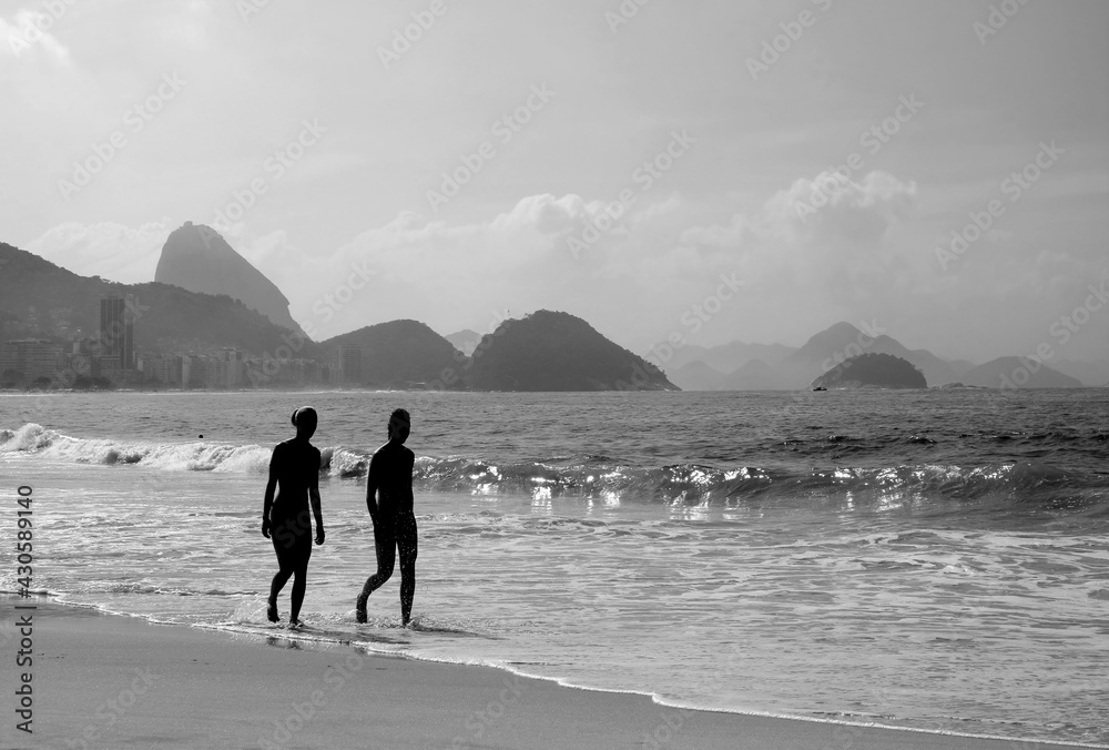 Silhouette of two young women walking on the sandy beach in monochrome