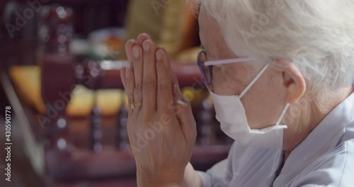An Asian old lady, a Buddhist, has white hair, wearing glasses and a mask to prevent COVID-19 , sitting and hands clasping, listen to Buddhist monks praying at the merit making ceremony in the temple. photo