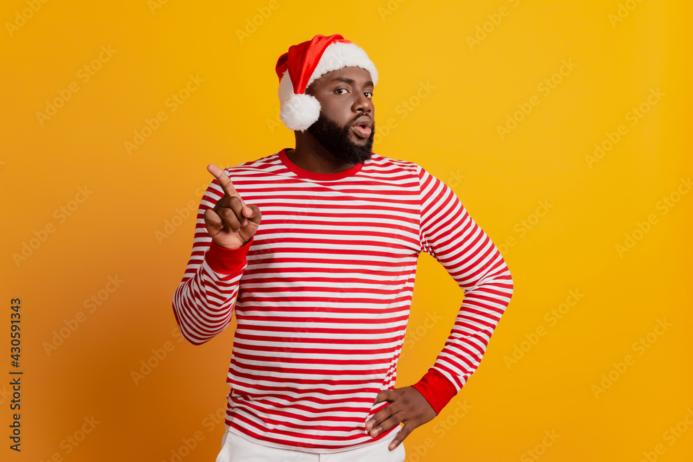 Portrait of angry guy in santa hat raise finger direct empty space isolated on yellow background