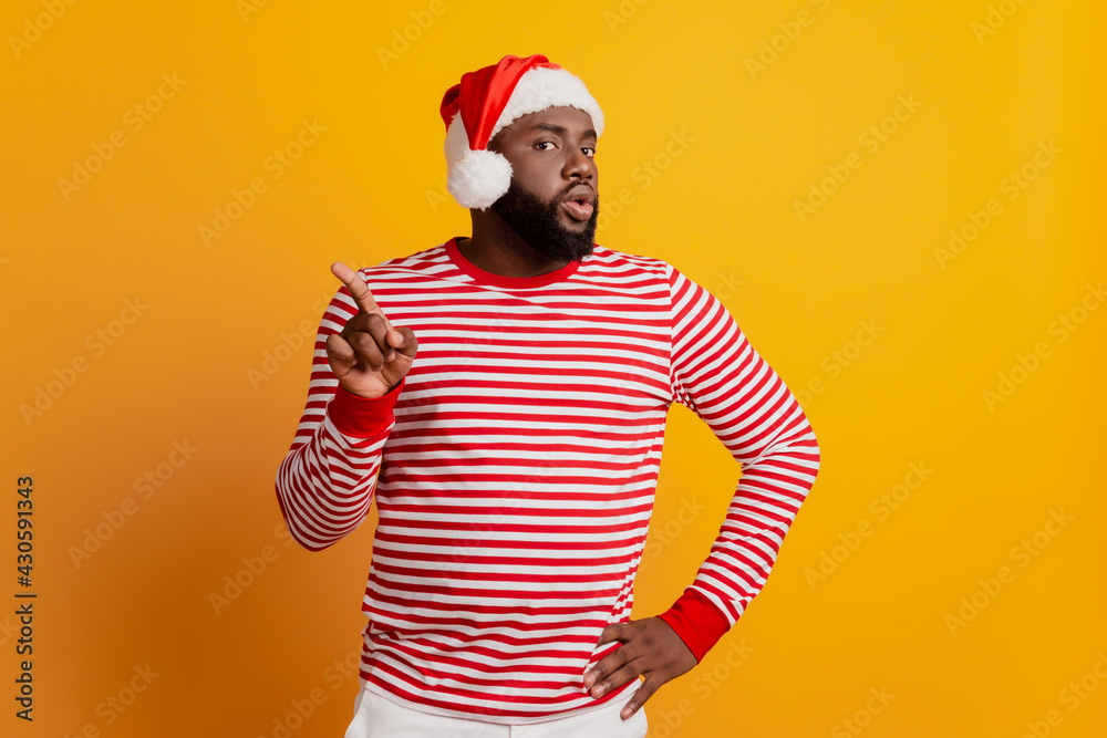 Portrait of angry guy in santa hat raise finger direct empty space isolated on yellow background Portrait of angry guy in santa hat raise finger direct empty space isolated on yellow background