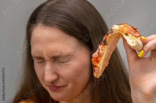 Fotografija Close-up of a young dark-haired woman holding a pizza in her hand in disgust with her eyes closed
