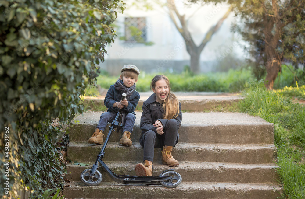 a boy and a girl sit on the steps with a scooter. they make faces and have fun. They're wearing vintage clothes. a boy and a girl sit on the steps with a scooter. they make faces and have fun. They're wearing vintage clothes.