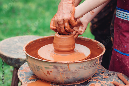 Pottery workshop outside. Master teaching kid to creating on the pottery wheel. Craftsman's hands and child