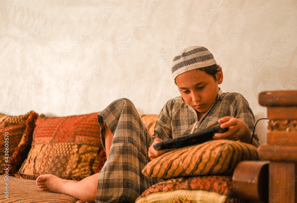 Fototapeta premium A boy of 8 years in Moroccan national clothing - djellaba, plays in the console.