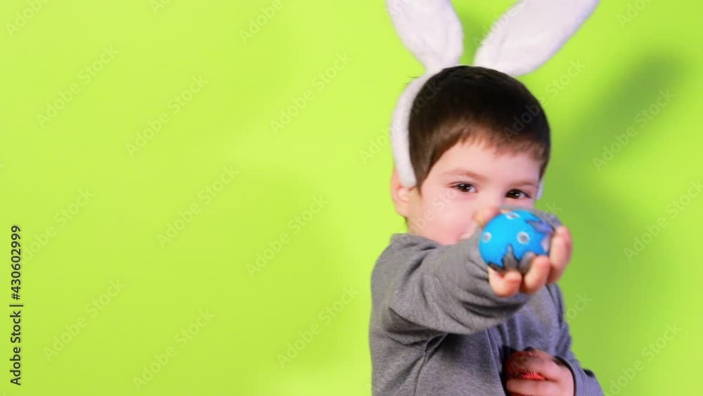 Happy joyful boy 3-4 years old with bunny ears on his head in a gray jacket plays with colorful eggs, shows easter eggs on a yellow studio background. Easter baby. Happy joyful boy 3-4 years old with bunny ears on his head in a gray jacket plays with colorful eggs, shows easter eggs on a yellow studio background. Easter baby.