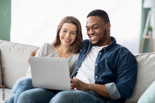 Weekend Pastime. Interracial Couple With Laptop Relaxing On Couch In Living Room
