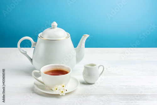 A cup of tea, a teapot and a milk jug on a white table.