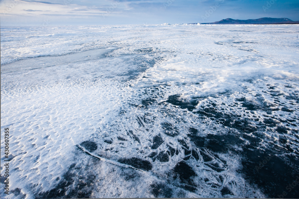Snow and ice on the flat surface of  Baikal under a blue sky in the distance mountain range