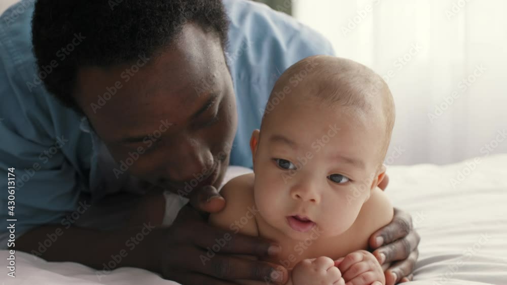 Cute infant lying on belly, loving african american father hugging and kissing his lovely baby, close up portrait Cute infant lying on belly, loving african american father hugging and kissing his lovely baby, close up portrait