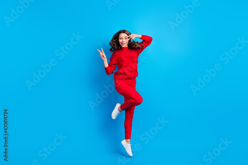 Full length body size photo of woman wearing casual outfit jumping high showing v-sign gesture isolated on vibrant blue color background