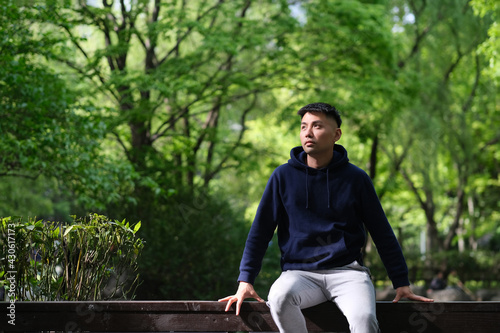 handsome Asian young man sitting in natural park, looking to the sunshine. Green forest background