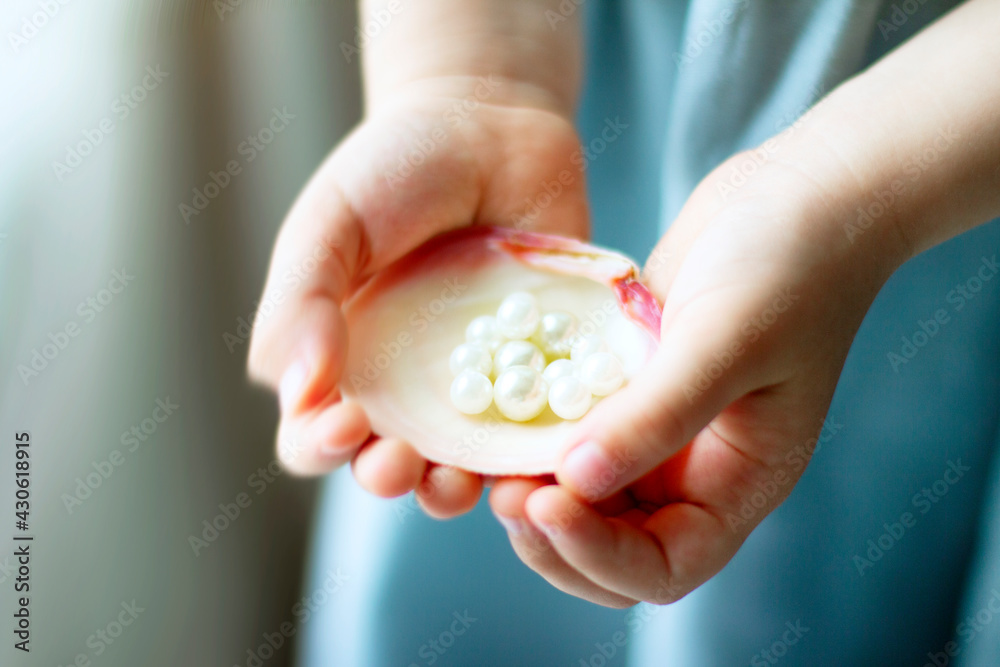 Children's hands hold oyster shell with pearls Children's hands hold oyster shell with pearls