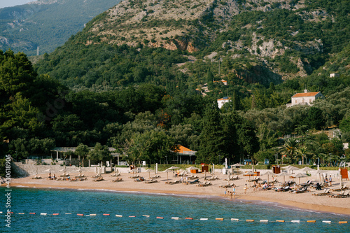 View of a beach with sun loungers and sun umbrellas in the background of Sveti Stefan island in Montenegro © Nadtochiy