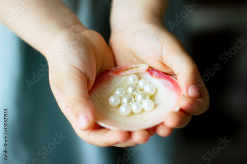 Children's hands hold oyster shell with pearls