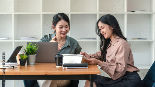 Two young Asian businesswoman are happy to work together using Laptop at the office.
