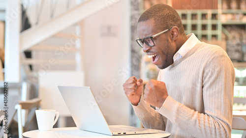 Excited African Man Celebrating Success on Laptop in Cafe