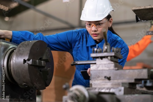 Portrait of engineer worker woman wearing uniform and PPE holding tablet and looking at machine in the factory. Preventive maintenance in factory. Industrial  technology and innovation concept.