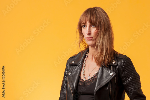 Titel: Portrait of an attractive woman wearing a black leather jacket against yellow background