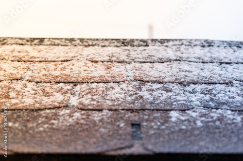 The sun warms up on the brown bituminous roof tile in the snow