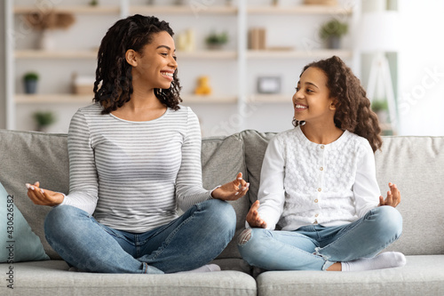 Cute black mother and daughter sitting on couch, meditating