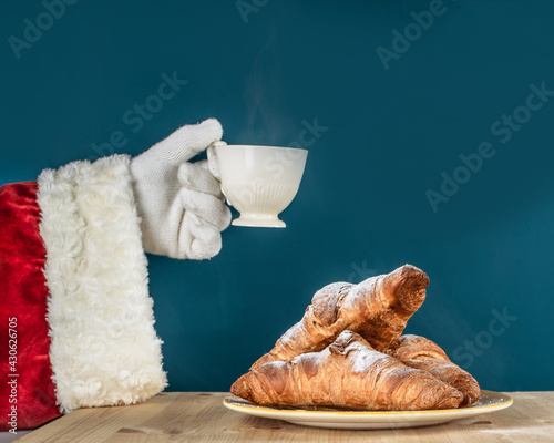 Hand of Santa Claus with a cup of coffee on a turquoise background. Delicious winter breakfast.