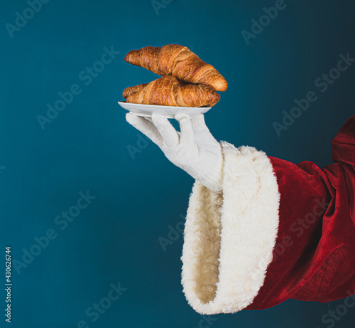 Hand of Santa Claus with croissants on a dark turquoise background with copy space.