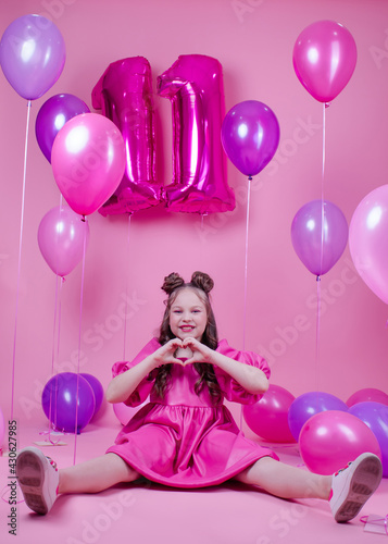 beautiful girl with pink make up and in pink leather dress. near colorful balloons in shape of number eleven 11. on pink background. concept of birthday party celebration.