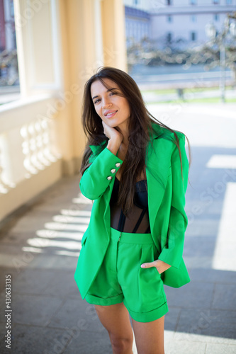 graceful caucasian female in a green suit and black blouse touch her hair and is staying in the shadow of arch of the ancient theater