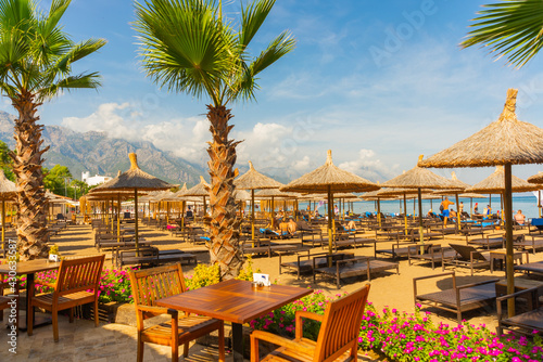 Fototapeta Naklejka Na Ścianę i Meble -  KEMER, TURKEY: Beach umbrellas and palm trees on the Central beach of Kemer, with mountains in the background.
