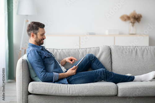 Relaxed bearded man using digital tablet at home