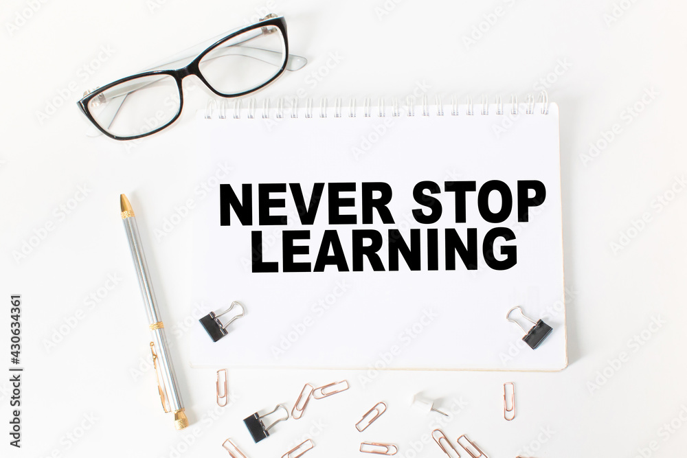 Notepad with text NEVER STOP LEARNING on the office desk with stationery. A blank notepad for entering a copy or text. business