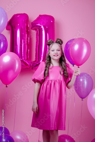 sweet brunette girl with pink make up and in pink leather dress. near colorful balloons in shape of number eleven. on pink background.concept of joy, party, birthday celebration.