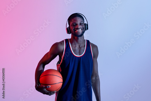 Hapy black basketball player listening to music, wearing headphones in neon lighting