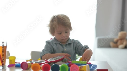 Cute blond child,  sweet boy, playing with play doh modeline at home, making different objects photo