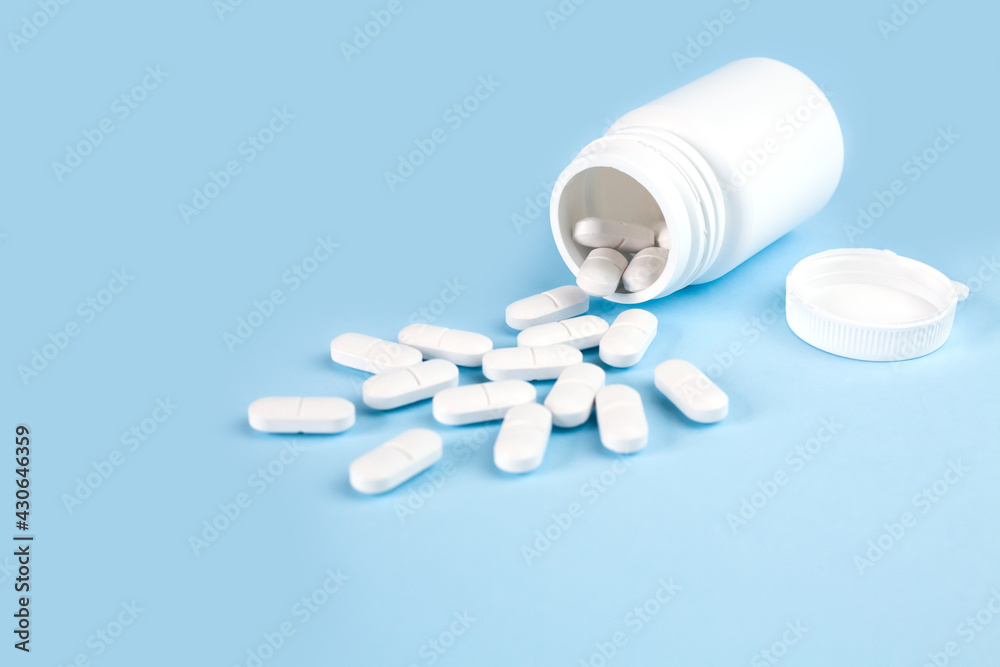 Scattered pills from the white bottle on blue background. Health care and medicine concept. Copy space. Close-up.