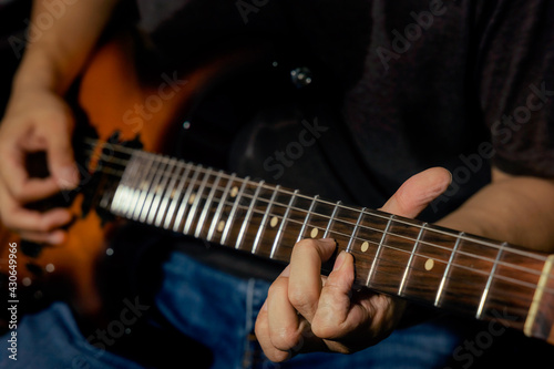 Closeup of male guitarist's hand and finger during playing guitar and a hand push on string on the guitar neck for chord while perform electric guitar lead solo. Rock l practice.