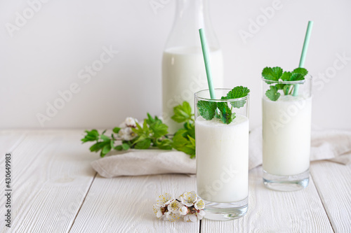 Fresh fermented milk chilled drink Lassi in two glasses on a white background with greenery and flowers.