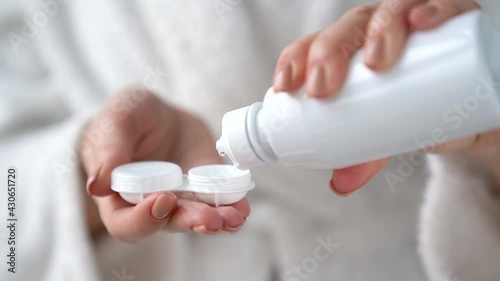 Closeup female hands are holding white plastic container for contact lenses. Woman is pouring cleaning liquid water for washing soft optical lens. Vision correction of myopia, hyperopia concept.