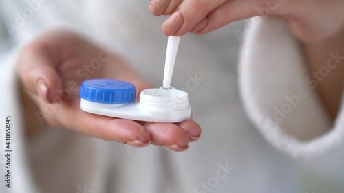 Closeup female hands are holding plastic container for contact lenses. Woman is washing soft optical lens in cleaning liquid, preparing to put in eye. Vision correction of myopia, hyperopia concept.