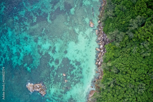 rone field of view of rocky coastline with cliffs meeting sea of turquoise blue Praslin Seychelles.