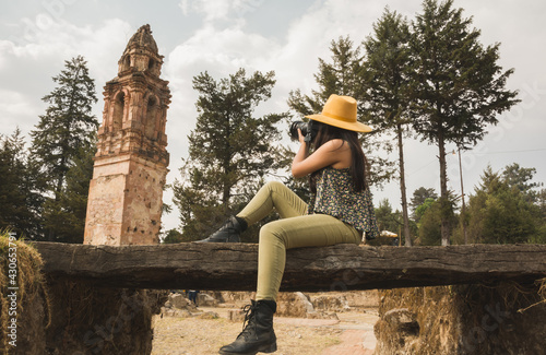 Adventurous girl with yellow hat taking photos in the ruins of an old church in the middle of the forest photo