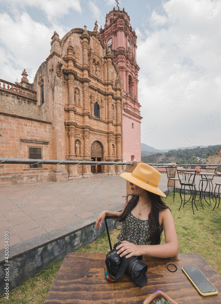 Adventurous girl with a yellow hat taking photos in the Magico town of Tlalpujahua, Michoacán, in the back is the main church of the place